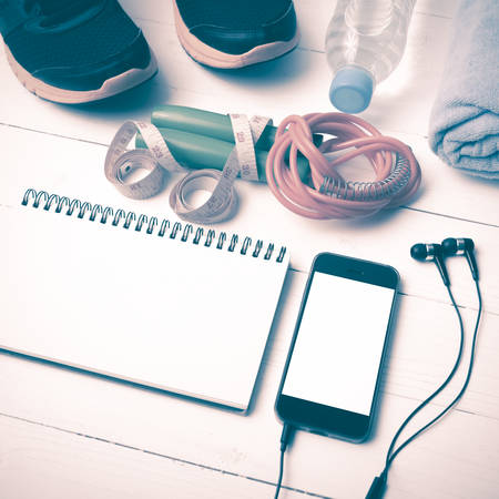 fitness equipment : running shoes,towel,jumping rope,water bottle,phone,notepad and measuring tape on white wood table vintage styleの写真素材