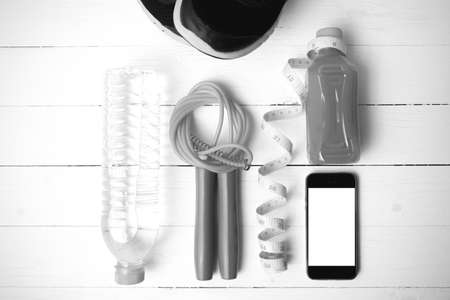 fitness equipment:running shoes,phone,measuring tape,water,juice and jumpong rope on white wood background black and white colorの写真素材