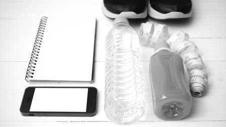 fitness equipment:running shoes,water,measuring tape,notepad,phone and juice on white wood...