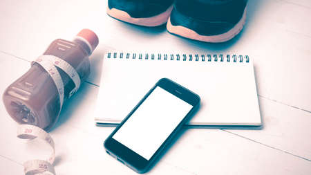 fitness equipment:running shoes,juice,measuring tape,notepad and phone on white wood background vintage styleの写真素材