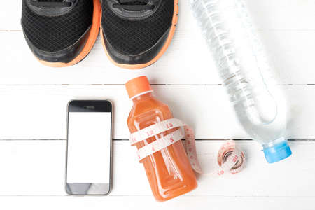 fitness equipment:running shoes,measuring tape,water,juice and phone on white wood background