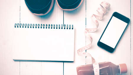 fitness equipment:running shoes,juice,measuring tape,notepad and phone on white wood background vintage styleの写真素材