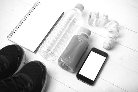 fitness equipment:running shoes,water,measuring tape,notepad,phone and juice on white wood...