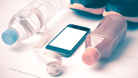 fitness equipment:running shoes,measuring tape,water,juice and phone on white wood background vintage styleの写真素材