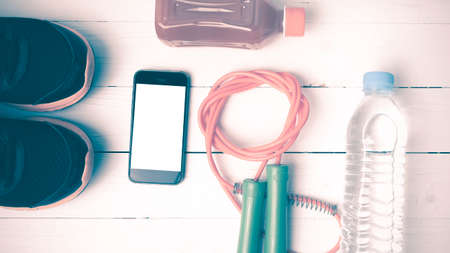 fitness equipment : running shoes,jumping rope,water,juice and phone on white wood background...