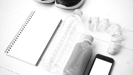 fitness equipment:running shoes,water,measuring tape,notepad,phone and juice on white wood...