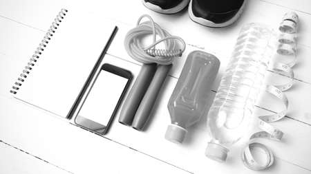 fitness equipment:running shoes,jumping rope,notepad,phone,water,juice and measuring tape on white wood background black and white colorの写真素材