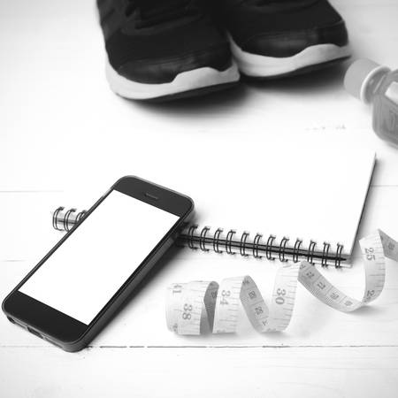 fitness equipment:running shoes,juice,measuring tape,notepad and phone on white wood background black and white colorの写真素材