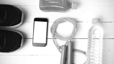 fitness equipment : running shoes,jumping rope,water,juice and phone on white wood background black and white colorの写真素材