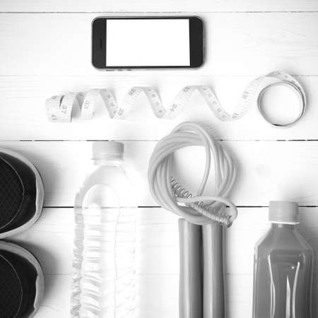 fitness equipment:running shoes,phone,measuring tape,water,juice and jumpong rope on white wood background black and white colorの写真素材