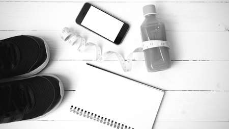 fitness equipment:running shoes,juice,measuring tape,notepad and phone on white wood background black and white colorの写真素材