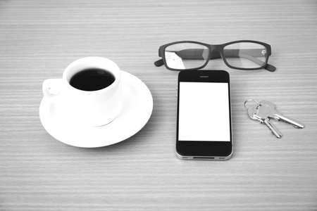 coffee cup and phone with key on wood background black and white colorの写真素材