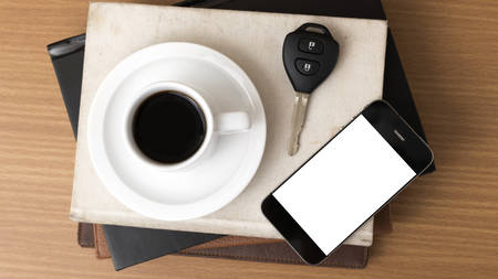 coffee cup with phone car key and stack of book on wood backgroundの写真素材