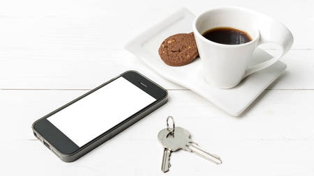 coffee cup with cookie,phone and key on white wood table