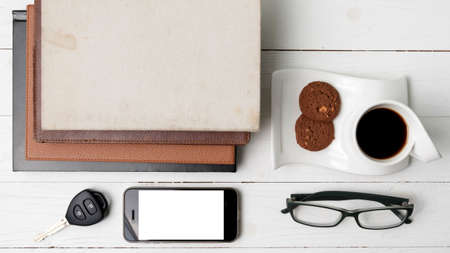 coffee cup with cookie,phone,stack of book and car key on white wood tableの写真素材
