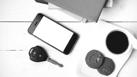 coffe cup with cookie,phone,car key and stack of book on white wood table black and white color