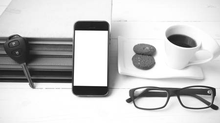 coffee cup with cookie,phone,stack of book and car key on white wood table black and white colorの写真素材