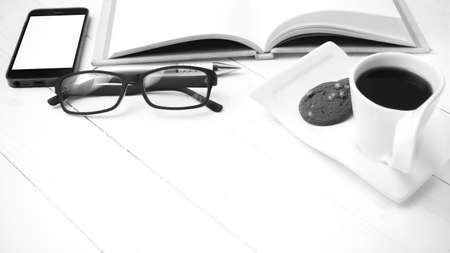 coffee cup with cookie,phone,notebook and eyeglasses on white wood table black and white colorの写真素材