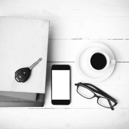 coffee cup with phone, car key,eyeglasses and stack of book on white wood table black and white colorの写真素材