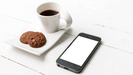 coffee cup with cookie and phone on white wood background