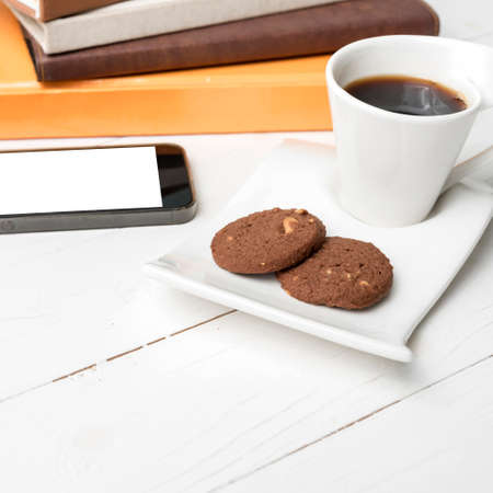 coffe cup with cookie,phone and stack of book on white wood table