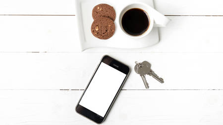 coffee cup with cookie,phone and key on white wood tableの写真素材