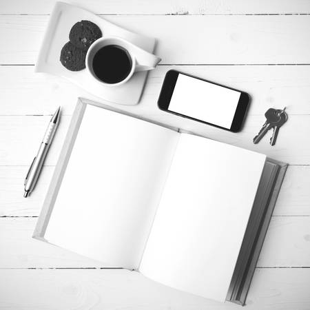 coffee cup with cookie,phone,notebook and key on white wood table black and white colorの写真素材