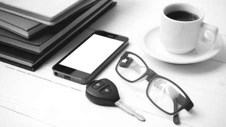 coffee cup with phone, car key,eyeglasses and stack of book on white wood table black and white colorの写真素材