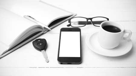 coffee cup with phone, car key,eyeglasses and open notebook on white wood table black and white colorの写真素材