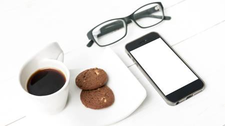 coffee cup with cookie,phone and eyeglasses on white wood tableの写真素材