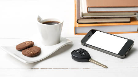 coffe cup with cookie,phone,car key and stack of book on white wood tableの写真素材