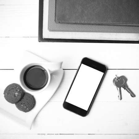 coffee cup with cookie,phone,stack of book and key on white wood table black and white colorの写真素材