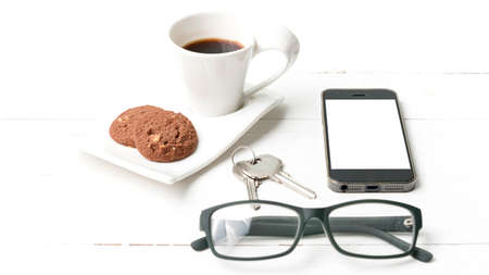 coffee cup with cookie,phone,eyeglasses and key on white wood background