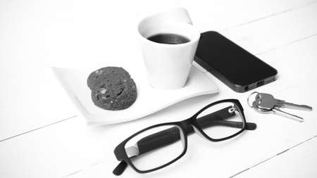 coffee cup with cookie,phone,eyeglasses and key on white wood background black and white color