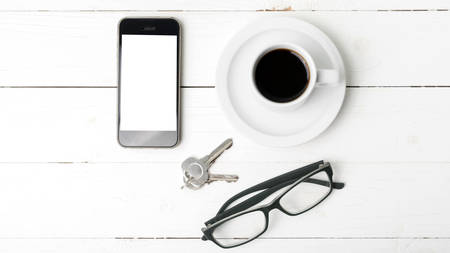 coffee cup with phone, eyeglasses and key on white wood tableの写真素材