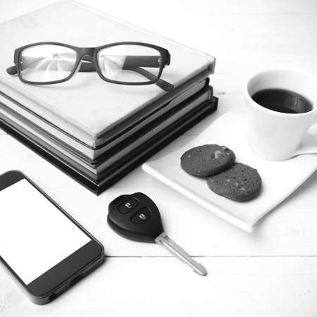 coffee cup with cookie,phone,stack of book and car key on white wood table black and white colorの写真素材