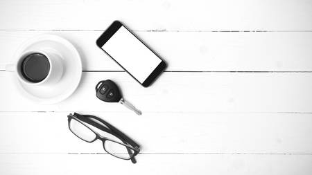 coffee cup with phone, eyeglasses and car key on white wood table black and white colorの写真素材