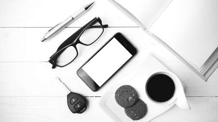 coffee cup with cookie,phone,open notebook,car key and eyeglasses on white wood table black and...