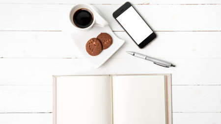 coffee cup with cookie,phone with notebook and pen on white wood table