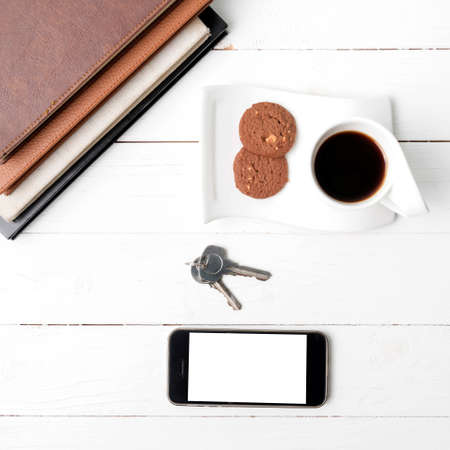 coffee cup with cookie,phone,stack of book and key on white wood tableの写真素材