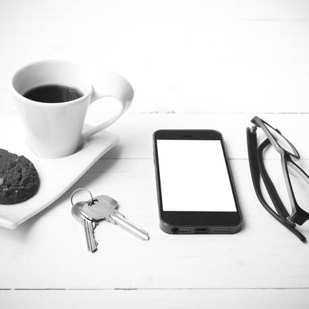 coffee cup with cookie,phone,eyeglasses and key on white wood background black and white colorの写真素材