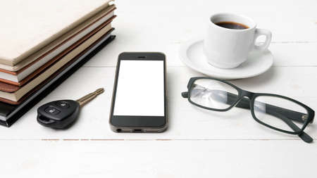 coffee cup with phone, car key,eyeglasses and stack of book on white wood tableの写真素材