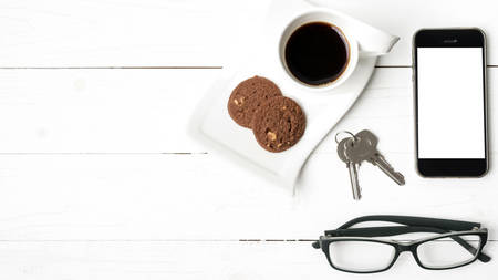 coffee cup with cookie,phone,eyeglasses and key on white wood background