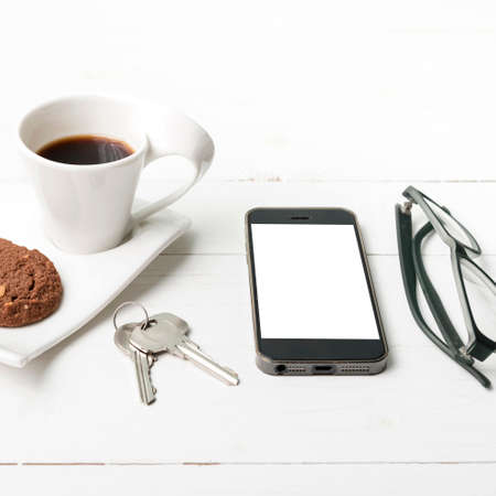 coffee cup with cookie,phone,eyeglasses and key on white wood backgroundの写真素材