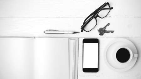 coffee cup with phone, key,eyeglasses and open notebook on white wood table black and white color