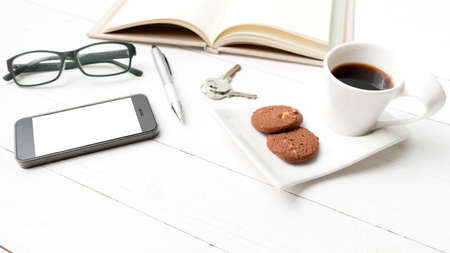 coffee cup with cookie,phone,open notebook and eyeglasses on white wood tableの写真素材
