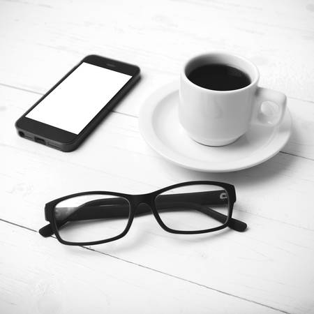 coffee cup with phone and eyeglasses on white wood table black and white color