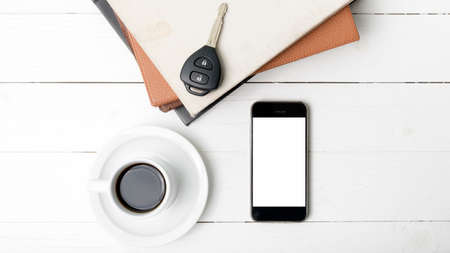 coffee cup with phone,car key and stack of book on white wood tableの写真素材