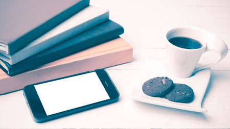 coffe cup with cookie,phone and stack of book on white wood table vintage styleの写真素材