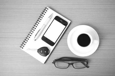 coffee,phone,notepad,eyeglasses and car key on wood table background black and white colorの写真素材